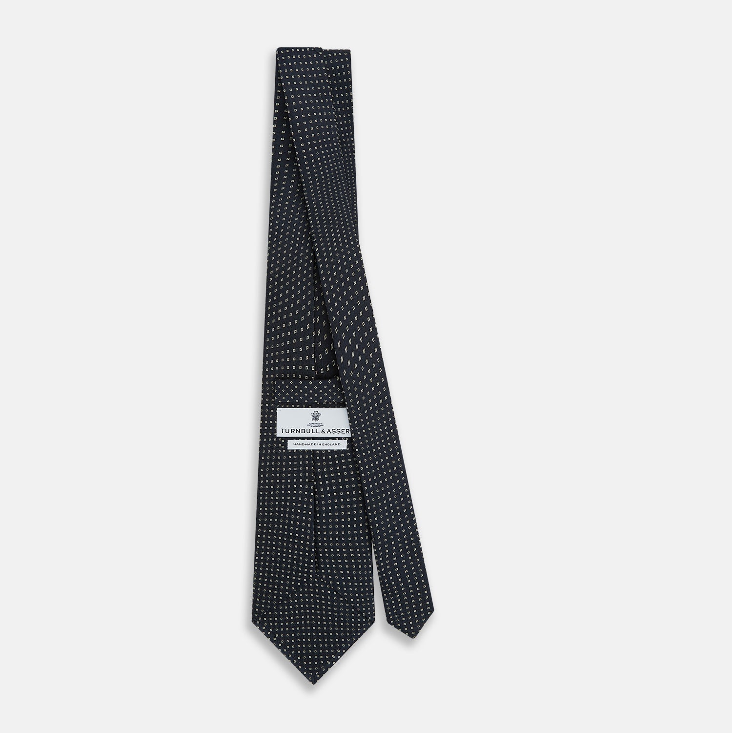 View 4 of product The Navy and White Square Silk Tie by Turnbull & Asser is crafted from English silk with a subtle white square pattern, rolled tip-forward and displayed on a white background for a tailored look.