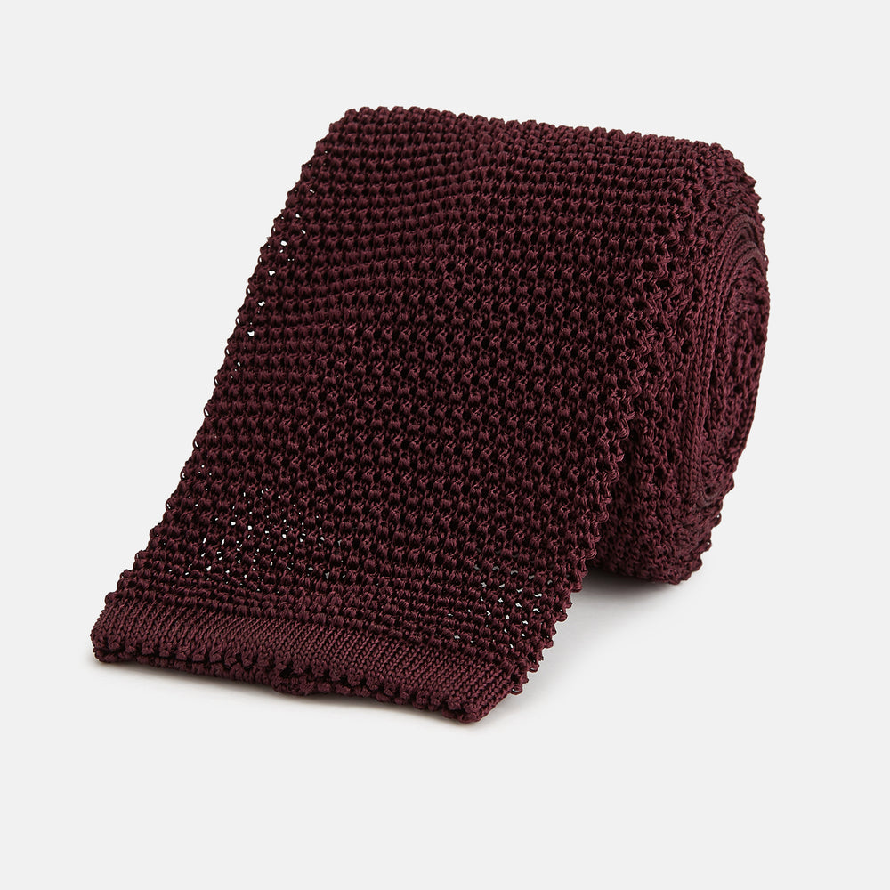The Turnbull & Asser Knitted Burgundy Square Silk Plain Tie, featuring a textured open-weave pattern, is rolled up and displayed on a plain white background—a versatile accessory for the modern gentleman.