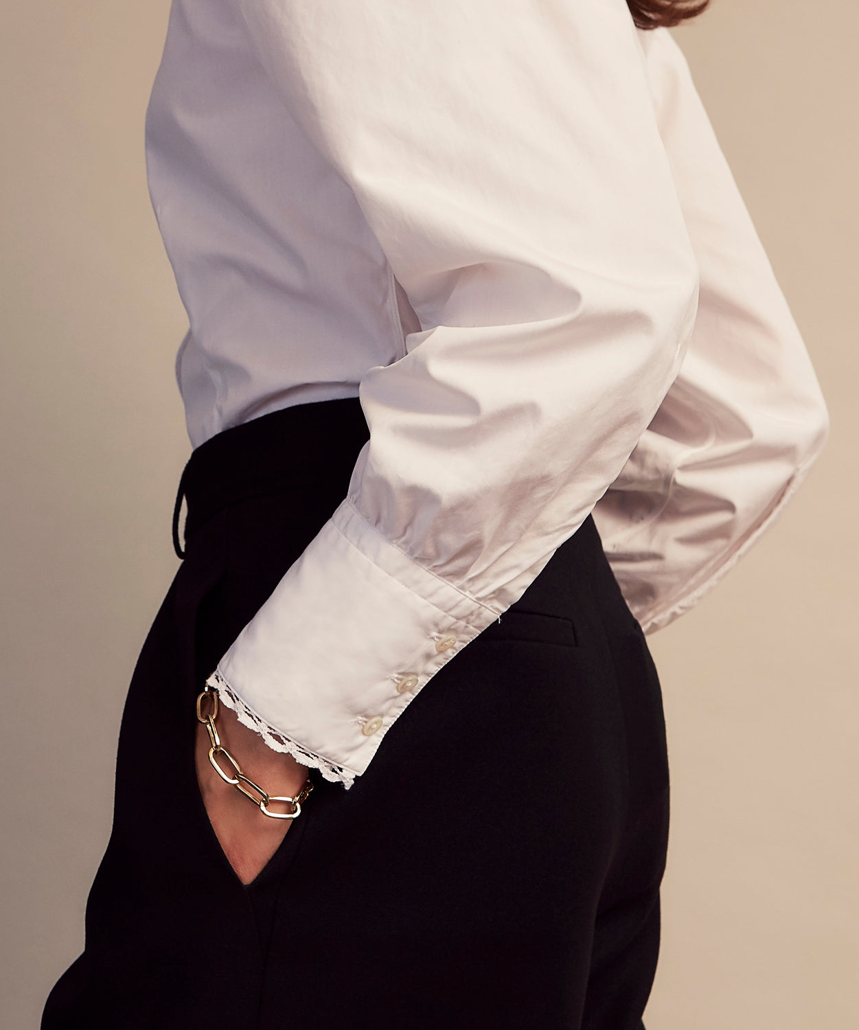 View 7 of product A woman stands in profile, looking down with hands in her pockets, wearing the Turnbull & Asser Turnbull and The Deck White Cotton Expressionist Shirt, paired with high-waisted black-and-white houndstooth pants.