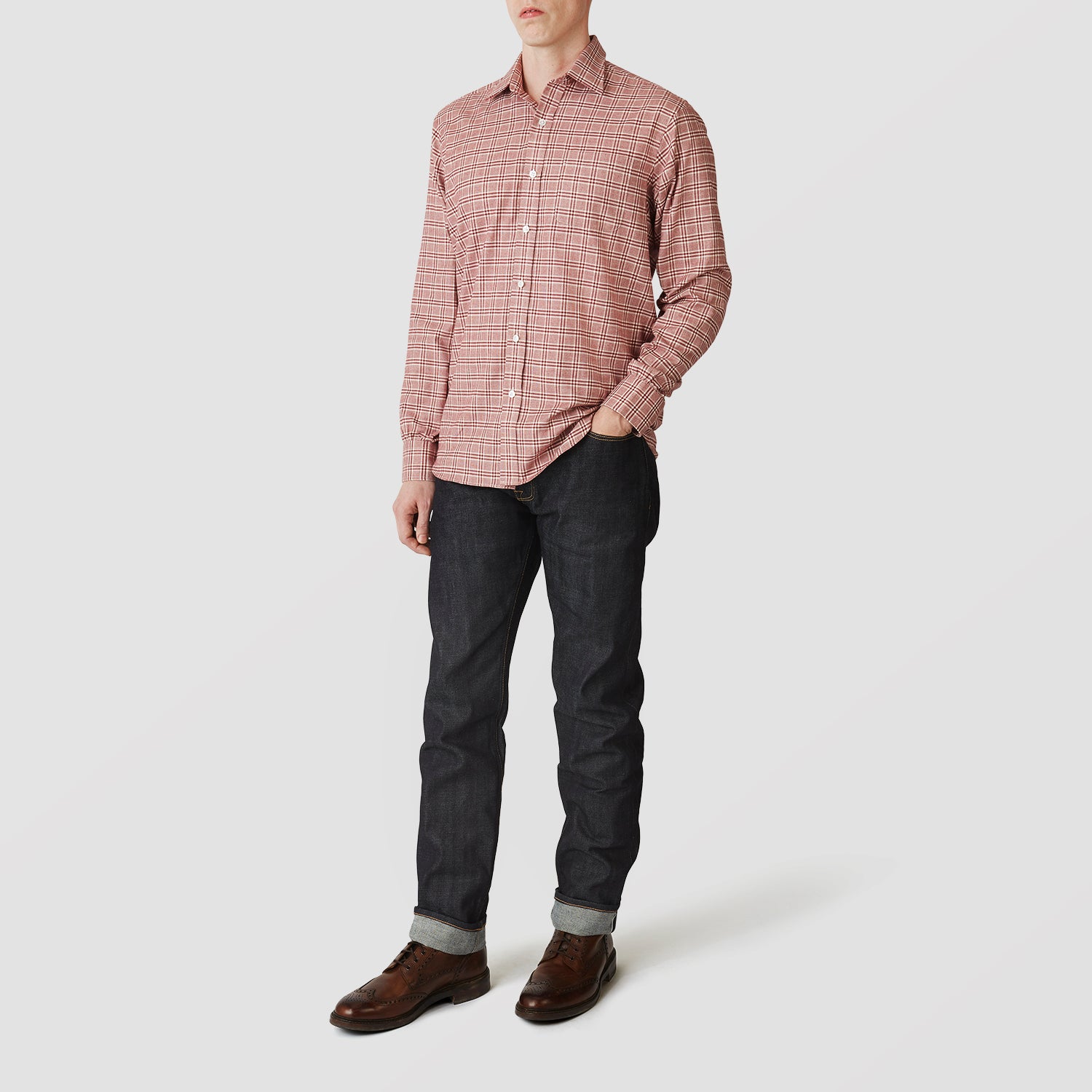 View 1 of product A person in a Turnbull & Asser Red Check Weekend Fit Shirt with a Derby collar and 1-button cuffs, paired with dark cuffed jeans and brown shoes, stands against a plain light background for an ideal winter layered style.