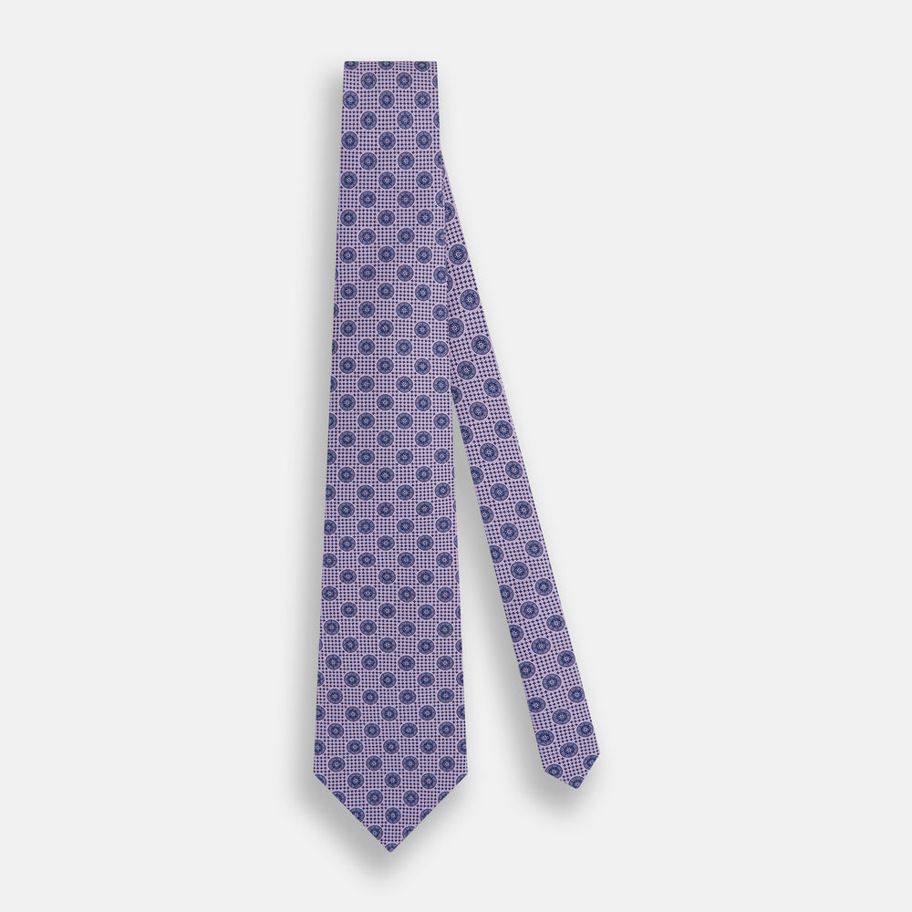 The Turnbull & Asser Lilac Medallion Printed Silk Tie is crafted from English silk with a geometric motif of small blue circles and a subtle checkered background.
