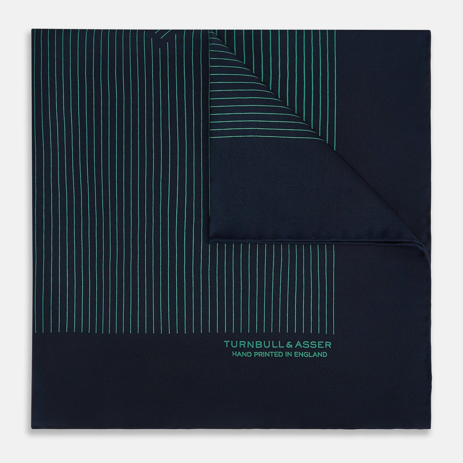 View 1 of product A Navy and Petrol Green Stripe Silk Pocket Square by Turnbull & Asser, featuring thin petrol green stripes and "Turnbull & Asser Hand Printed in England" in the bottom right corner. One corner is folded to display hand-rolled edges.