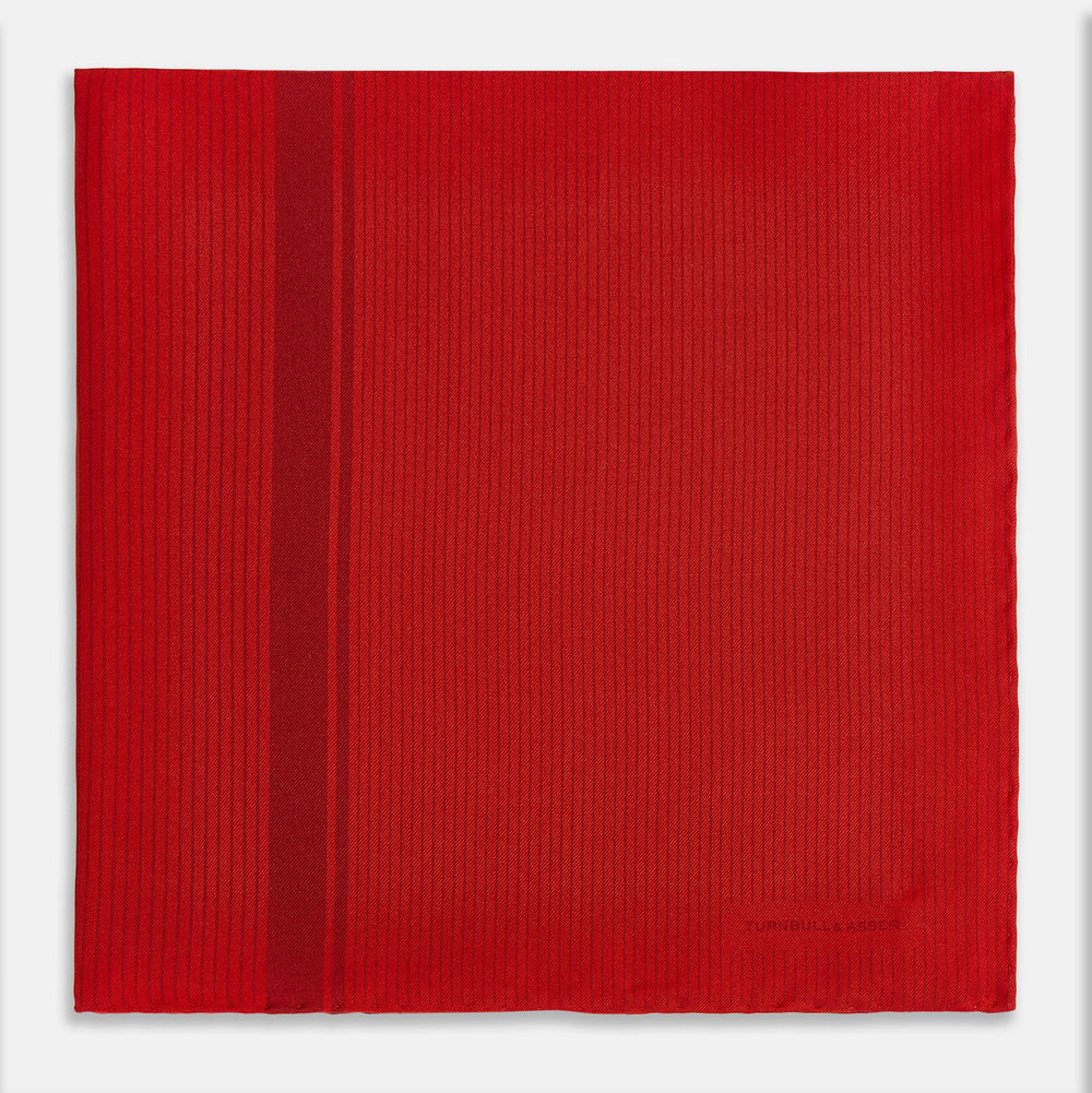 The Red and Burgundy Stripe Silk Pocket Square by Turnbull & Asser features subtle vertical stripes and a darker red stripe along one side, with “Turnbull & Asser” embossed in the fabric and a textured, turned-down corner.