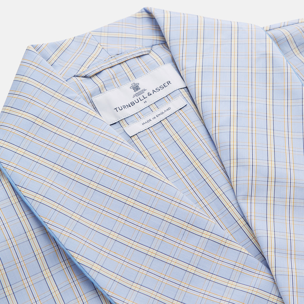 The Turnbull & Asser Blue and Yellow Check Poplin Cotton Dressing Gown features long sleeves, a shawl collar, front pockets, and a matching belt at the waist, shown on a plain white background.