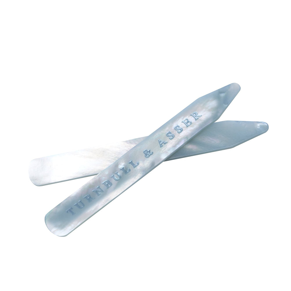 Two blue mother-of-pearl collar stays by Turnbull & Asser, ideal for keeping your shirt collar crisp; one is engraved with the brand name and both are displayed on a light gray background.