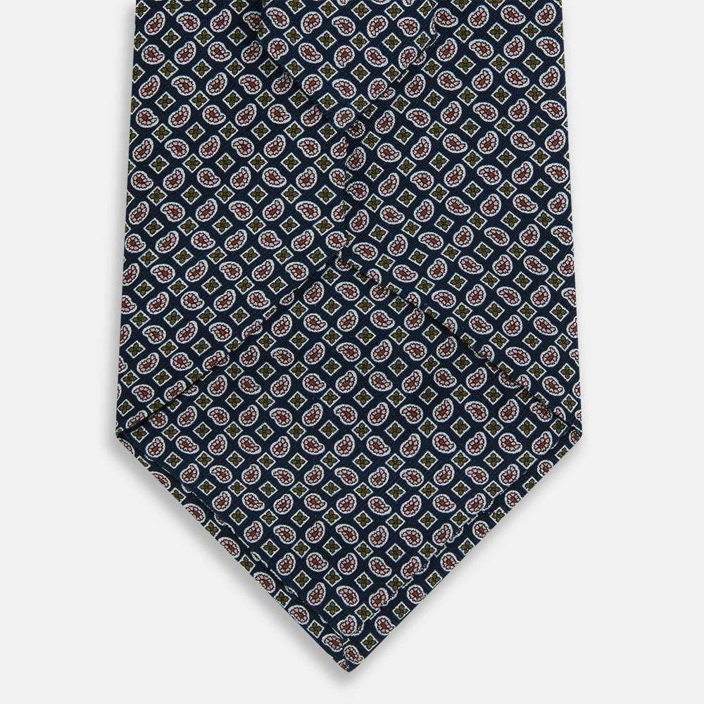 The Turnbull & Asser Navy Mélange Paisley and Square Print Silk Tie is crafted from fine silk, showcasing a repeating paisley and square pattern in blue tones, elegantly rolled for display on a white background.