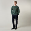 View 3 of product A man stands facing the camera against a plain light background, wearing the Turnbull & Asser Bottle Green Merino Kingston Crew Neck Jumper with dark pants and black shoes. His arms rest at his sides and he has a neutral expression.