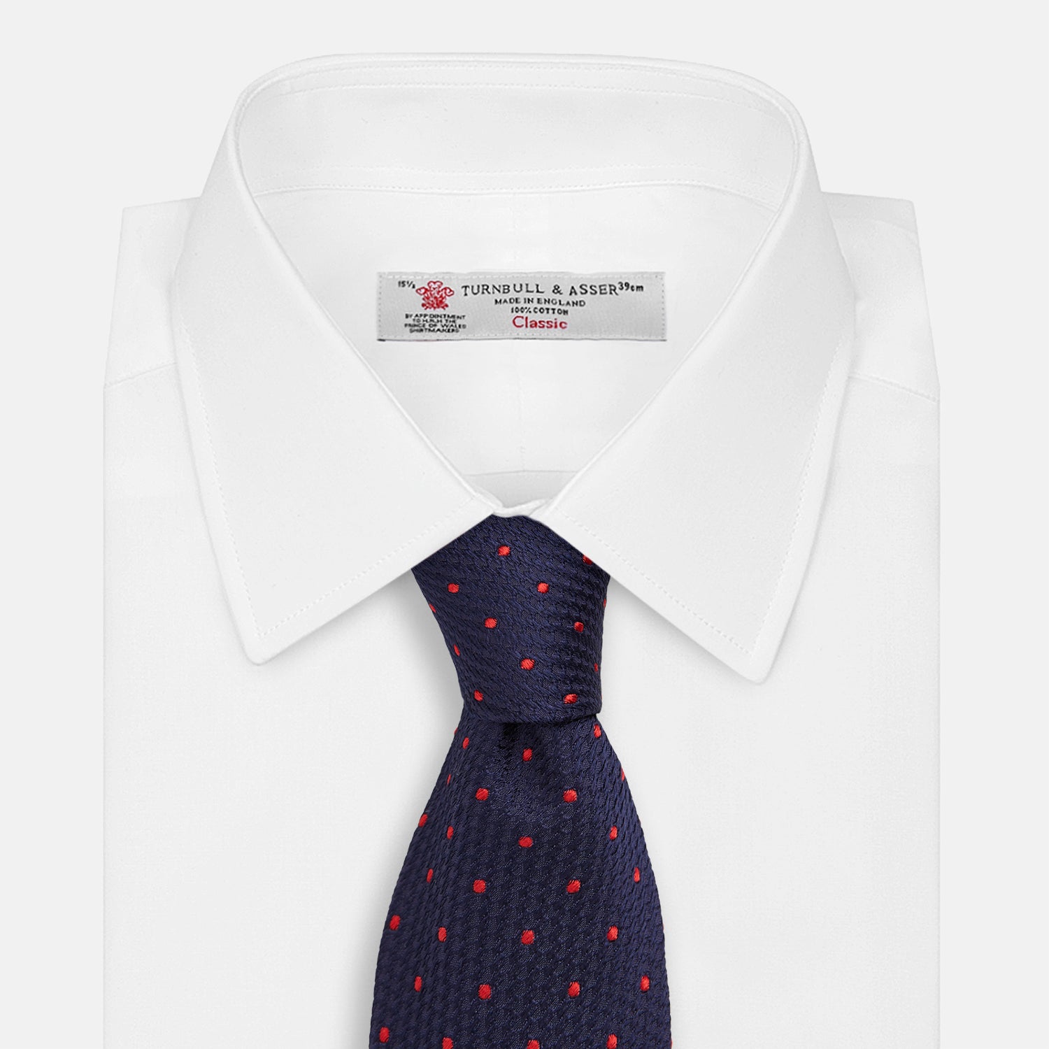 View 2 of product The Turnbull & Asser LACE ON TONE SPOT NAVY TULIP RED TIE is a classic men's accessory crafted from textured navy fabric with small red polka dots, neatly rolled with the pointed end facing forward.