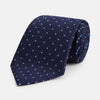 View 1 of product The LACE ON TONE SPOT NAVY FORD TIE by Turnbull & Asser is a rolled-up navy tie with textured fabric and an evenly spaced pattern of small light blue polka dots.