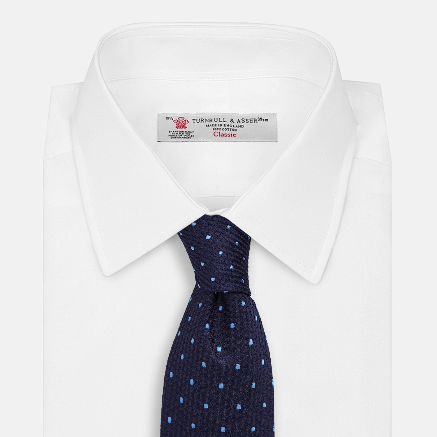 View 2 of product The LACE ON TONE SPOT NAVY FORD TIE by Turnbull & Asser is a rolled-up navy tie with textured fabric and an evenly spaced pattern of small light blue polka dots.