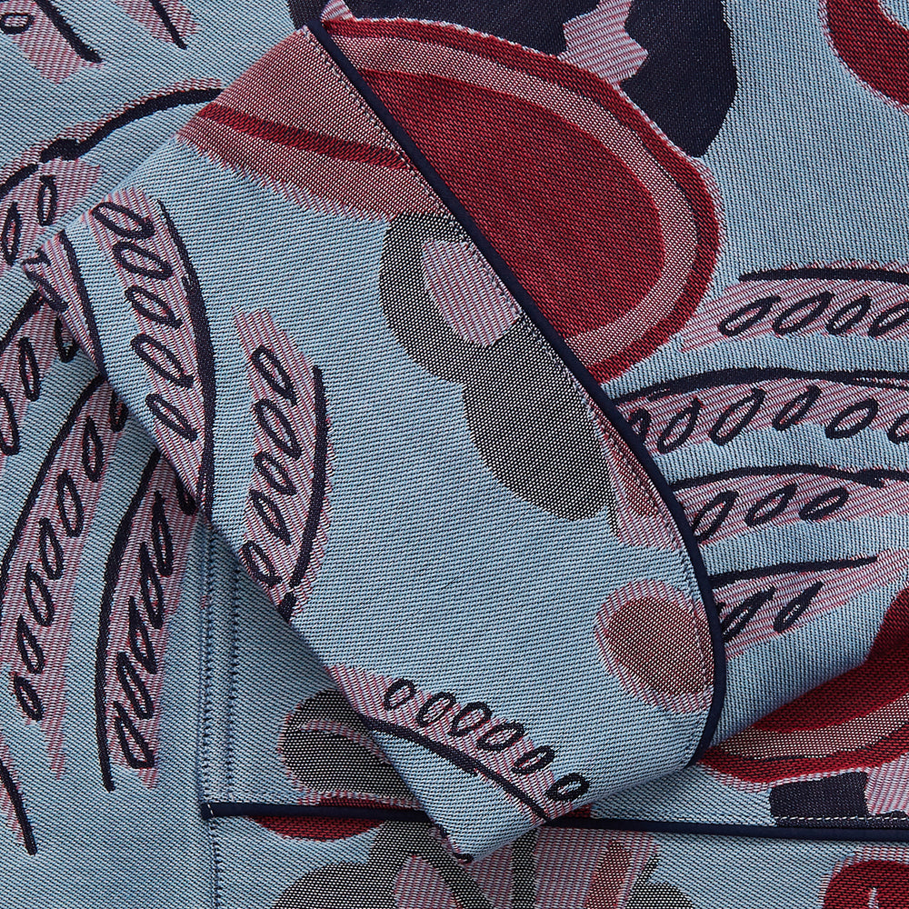 The Blue Paisley Pattern Cotton Arnold Gown by Turnbull & Asser features light blue jacquard cotton with a red and black paisley design, long sleeves, a matching belt, and two front pockets for a subtle Bloomsbury-inspired look.