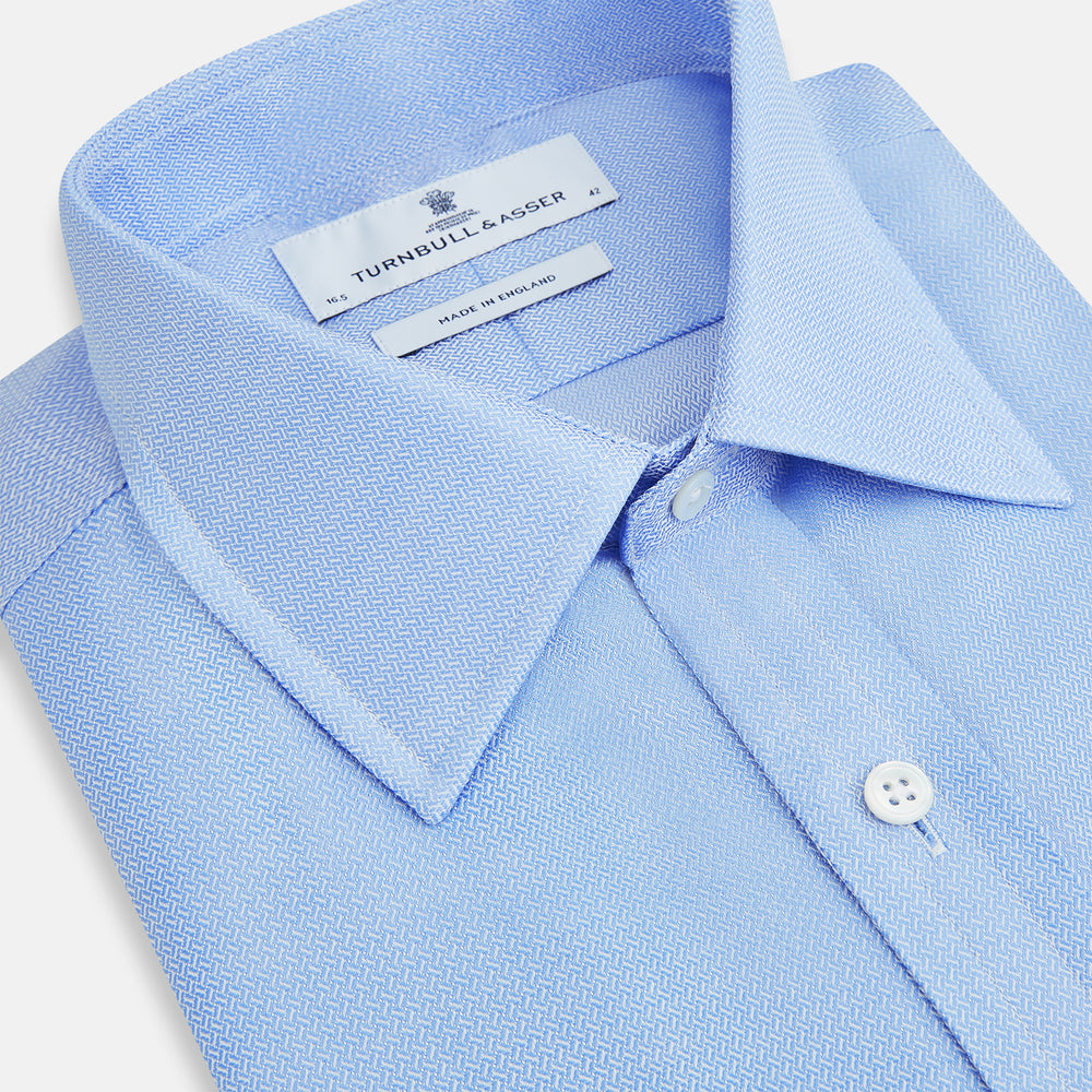 The Blue Herringbone Mayfair Shirt by Turnbull & Asser features light blue and white stripes, long sleeves, a classic collar, white buttons, and buttoned cuffs. Shown on a plain white background, it's perfect for formal occasions.