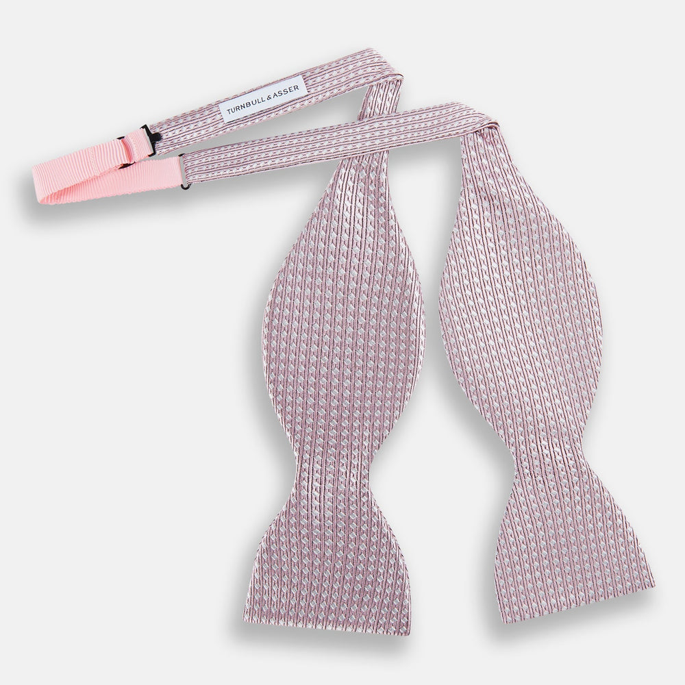 The Turnbull & Asser Pale Pink and White Square Silk Bow Tie features white stripes and subtle square patterns, ideal for formalwear. Shown on a white background.