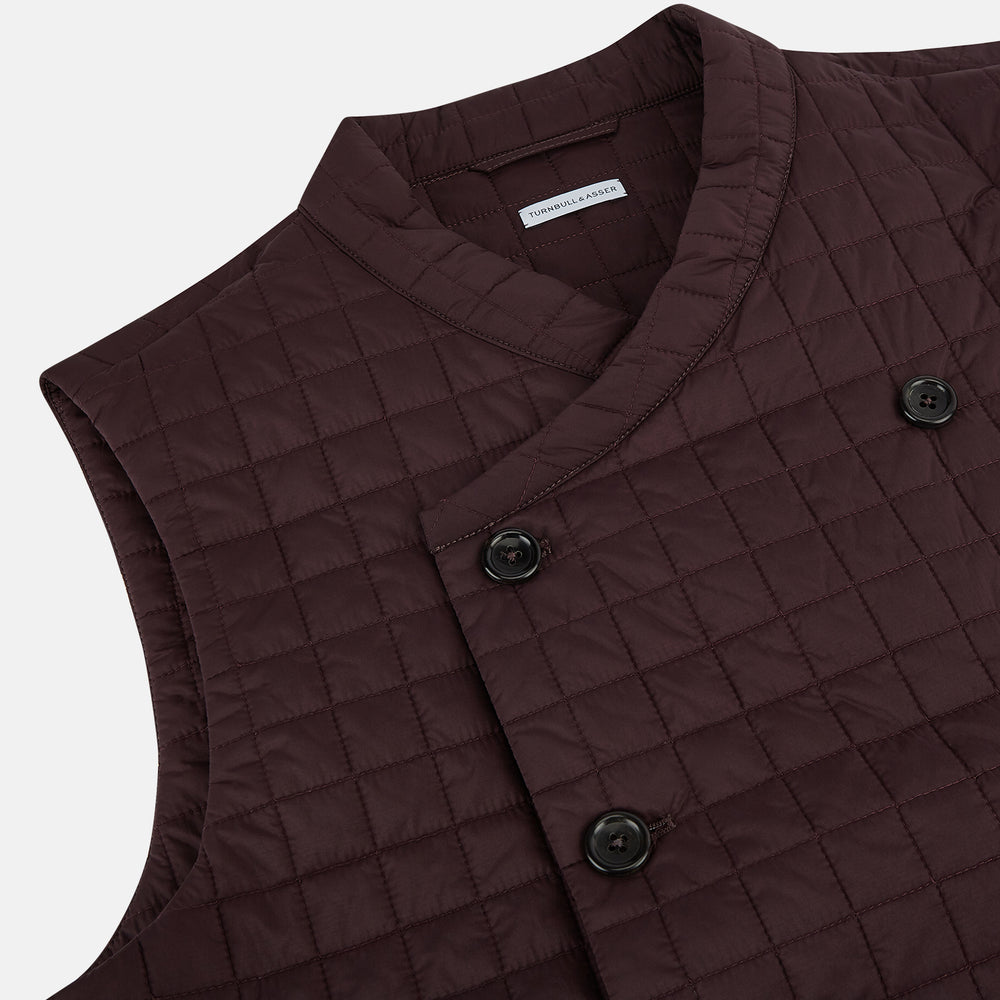 The Turnbull & Asser Burgundy Double-Breasted Quilted Gilet is a sleeveless vest with black buttons, an angled front, subtle check pattern, side and chest pockets—an ideal menswear piece for versatile layering.
