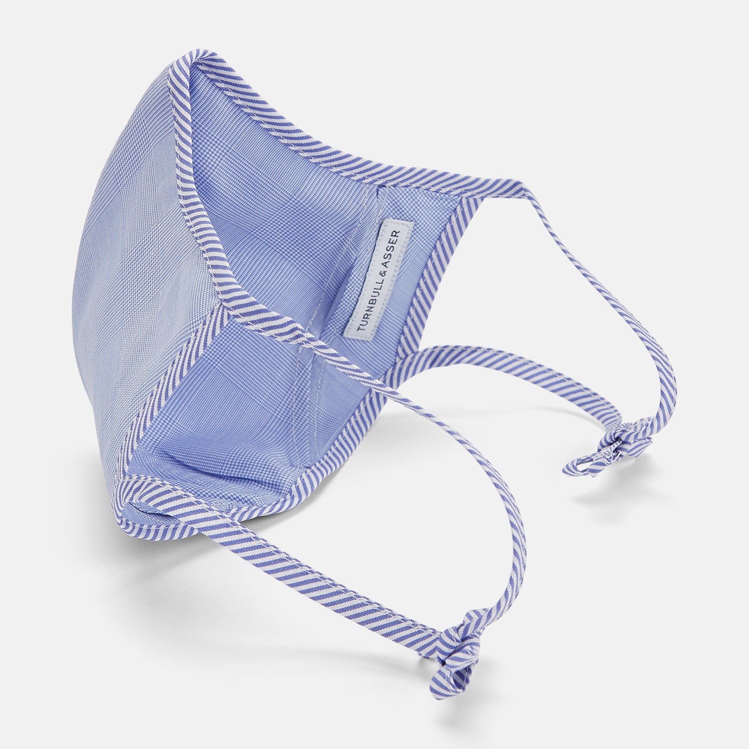 View 4 of product The Turnbull & Asser Blue Fine Check Zephyr Cotton Commuter Mask features a light blue and white check pattern, adjustable side ties, and comes with 3 Viroformula™ filters. Shown on a plain white background.