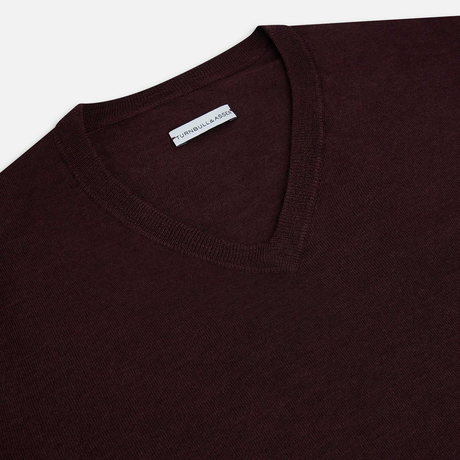 View 2 of product The Turnbull & Asser Burgundy Fine Merino V-Neck Jumper features a classic plain knit design with long sleeves, showcased against a crisp white background.
