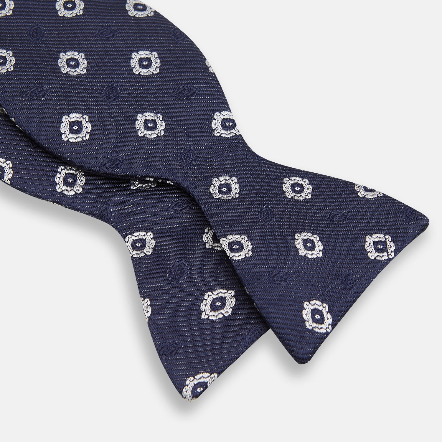 View 3 of product The Navy and White Motif Silk Bow Tie by Turnbull & Asser features a geometric floral pattern, adding refined elegance to formalwear. Shown on a plain white background.