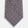 View 3 of product The Turnbull & Asser Ash Medallion Silk Tie is shown rolled up on a white background. This purple tie features a repeating geometric motif with small white circles and grid-like designs.