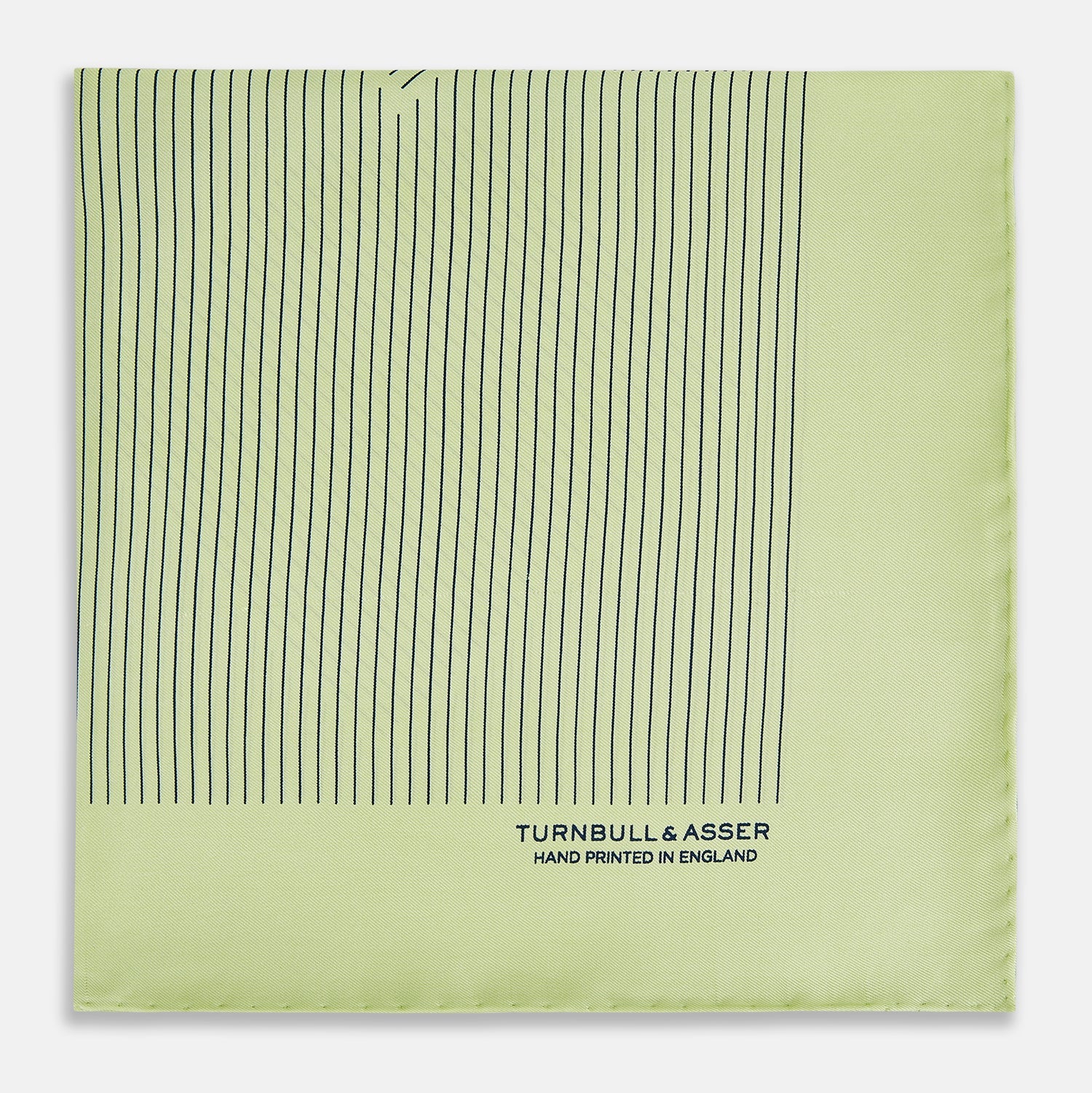 View 4 of product The Melon Green Stripe Silk Pocket Square by Turnbull & Asser features thin vertical black lines on light green silk, neatly folded to display both sides. The lower corner reads “TURNBULL & ASSER HAND PRINTED IN ENGLAND.”.