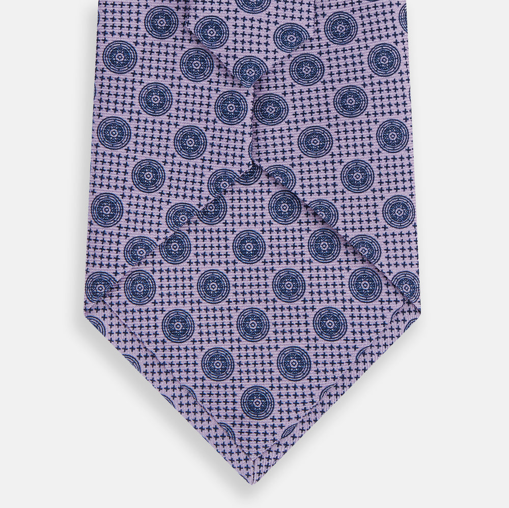 The Turnbull & Asser Lilac Medallion Printed Silk Tie is crafted from English silk with a geometric motif of small blue circles and a subtle checkered background.