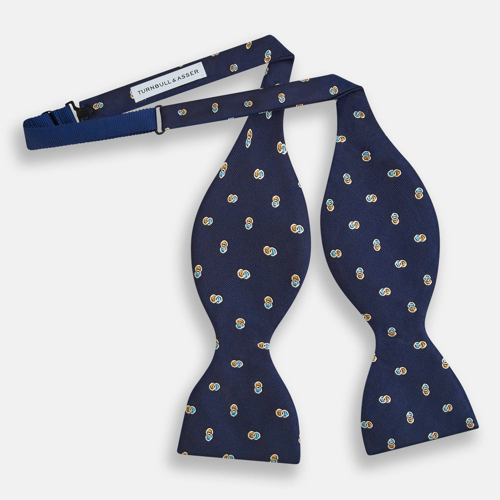 The Blue and Yellow Links Silk Bow Tie by Turnbull & Asser features a subtle wavy texture with a refined pattern of interlinked gold, blue, and white rings—an elegant accessory to enhance any formal outfit.