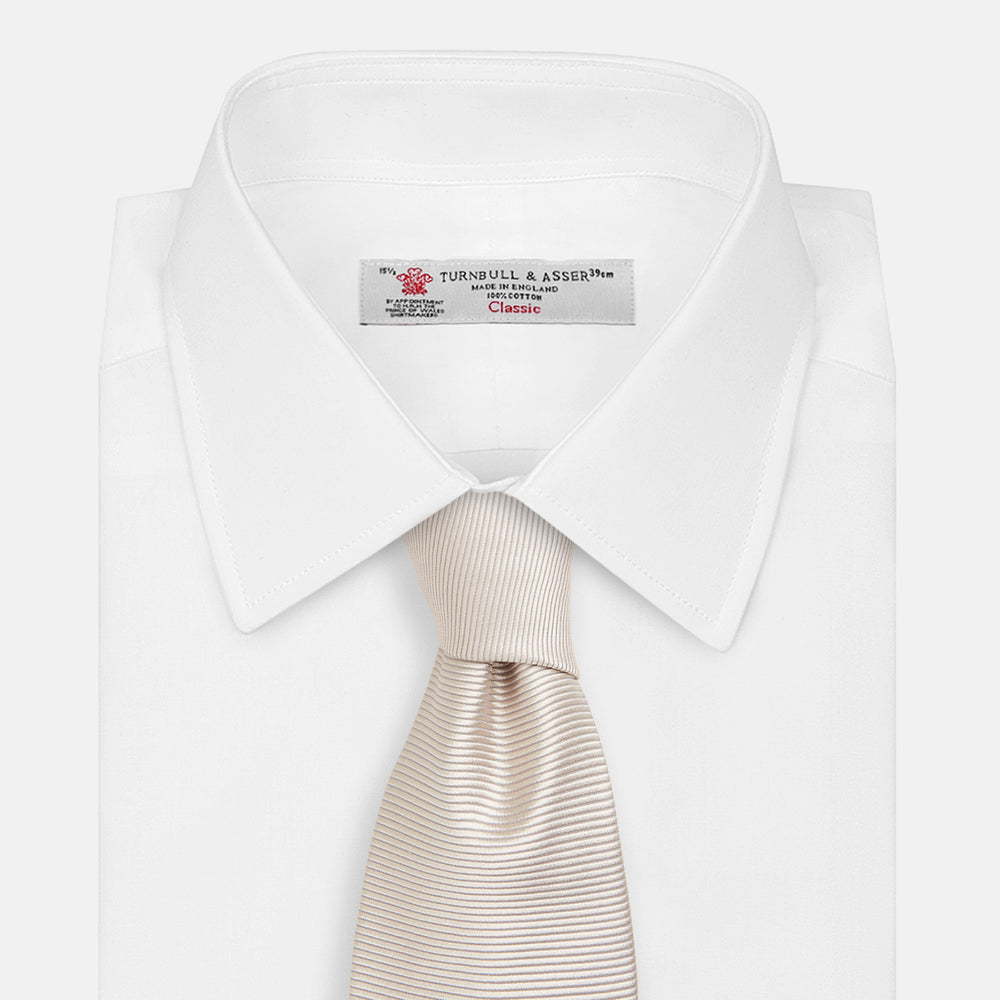 The Turnbull & Asser HORIZONTAL TWILL VELLUM TIE, a light beige silk necktie with a subtle ribbed texture, is shown rolled up on a white background—an essential finishing touch for smart attire.