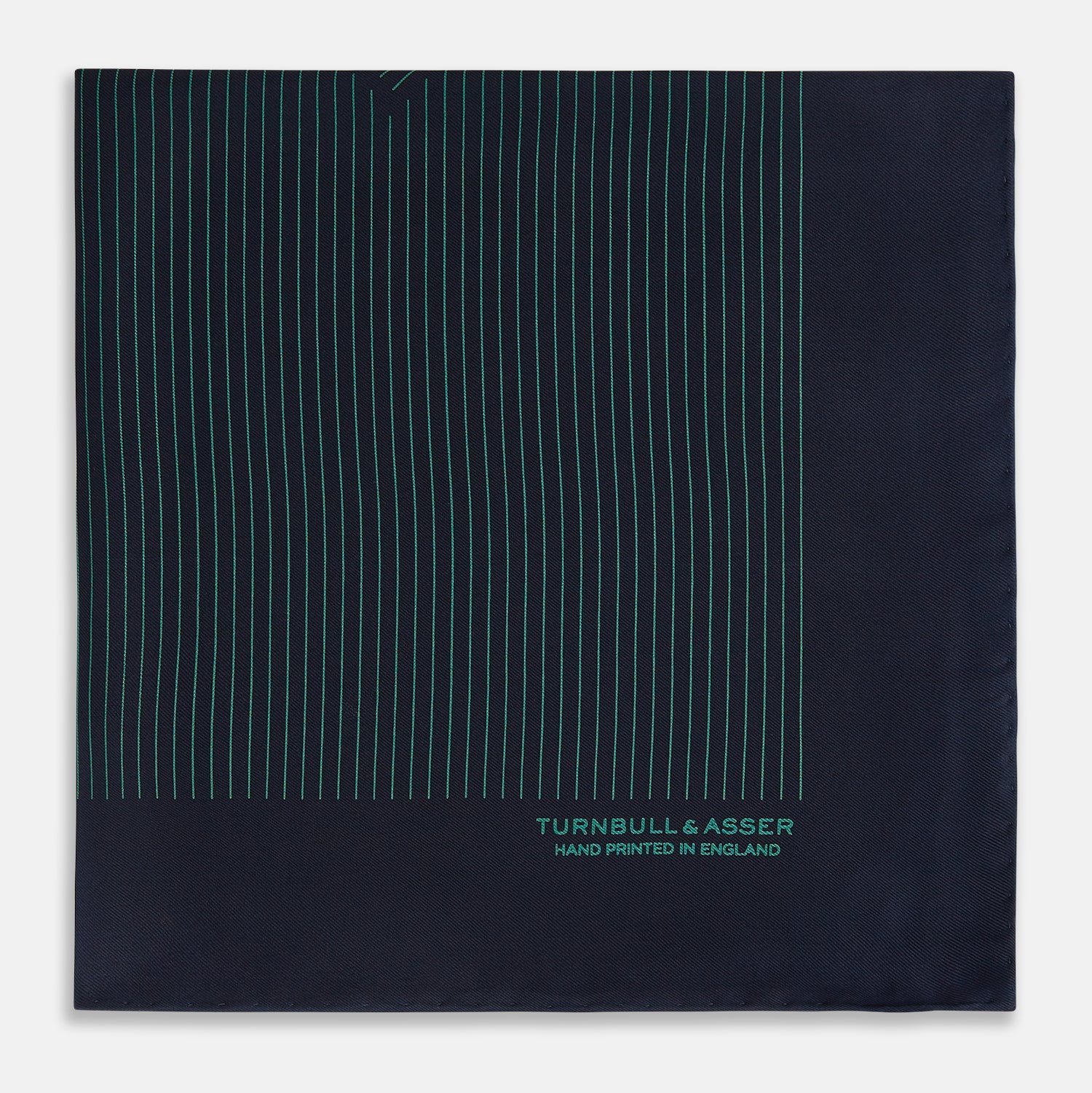 View 3 of product The Turnbull & Asser Navy and Hunter Green Stripe Silk Pocket Square features thin green stripes, hand-rolled edges, and "TURNBULL & ASSER HAND PRINTED IN ENGLAND" in green on the bottom right corner.
