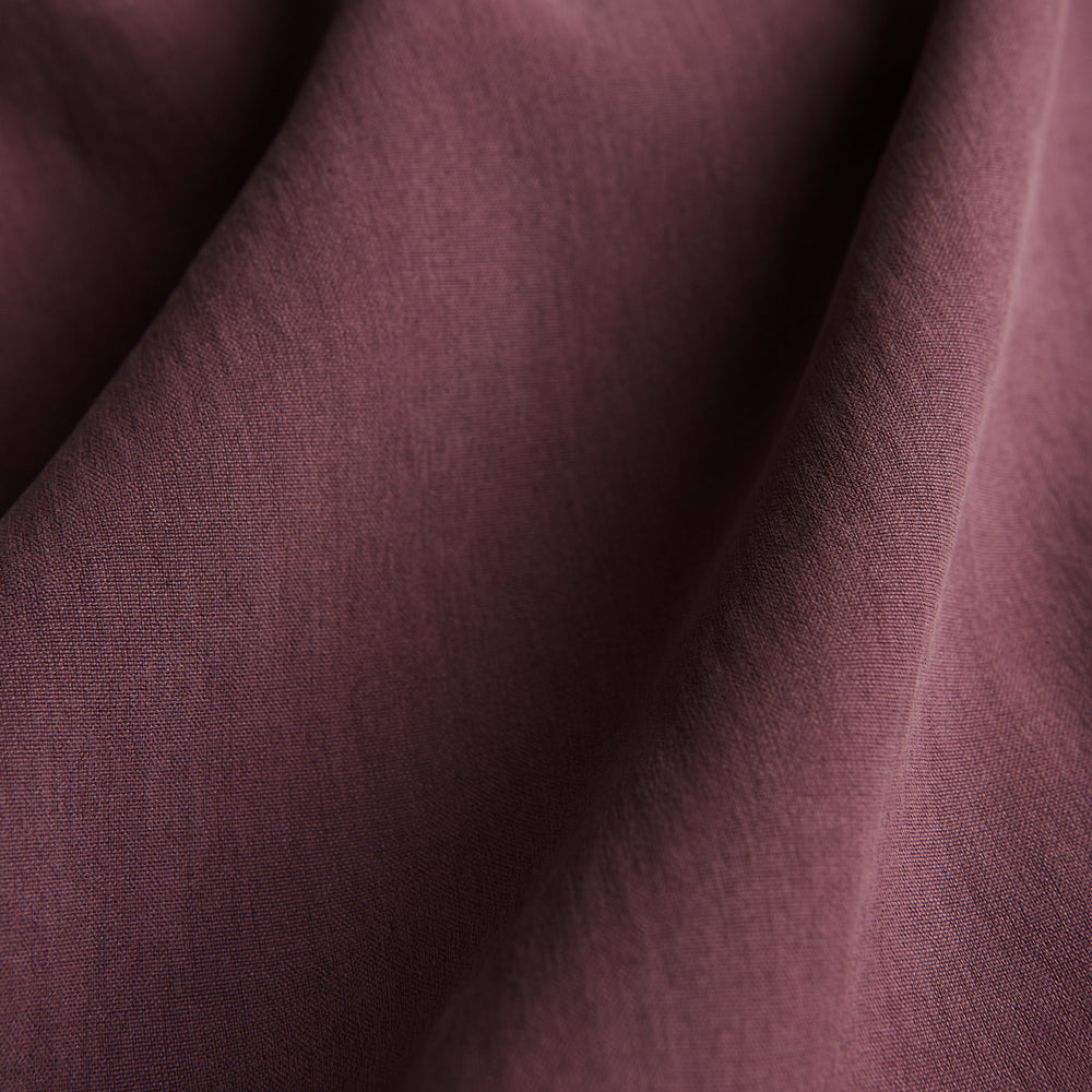 The Turnbull & Asser Plain Plum Silk Modern Pyjama Set, made in England, features white piping, a button-up long-sleeve top with three pockets, and matching pants. The pyjamas are shown against a white background.