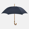 View 1 of product The Turnbull & Asser Navy Umbrella with Whangee Crook Handle is fully open, displaying its dark blue canopy and wooden curved handle against a plain white background.