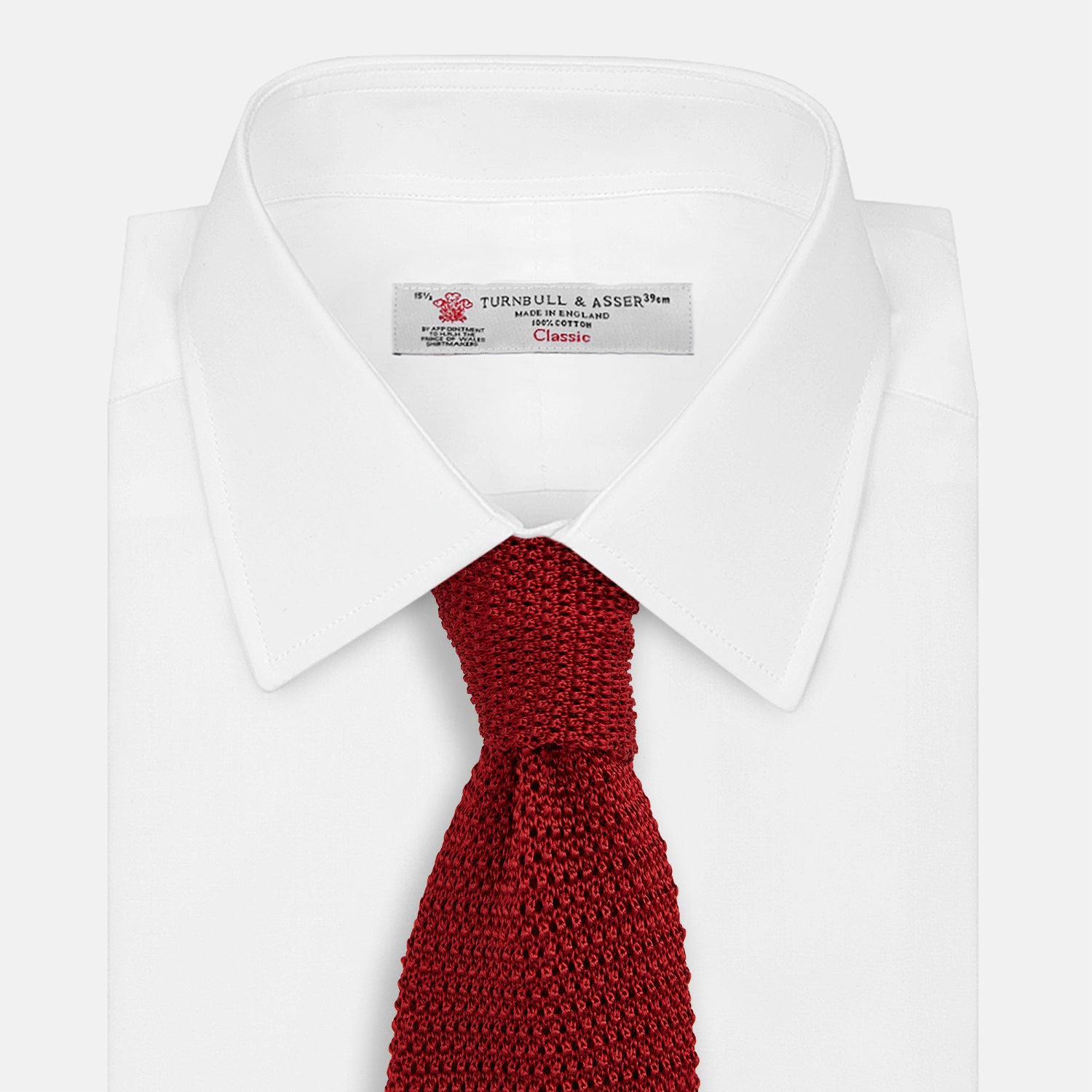 View 2 of product The Turnbull & Asser KNITTED RED SILK PLAIN TIE, featuring a textured finish, is rolled up and displayed against a plain white background.