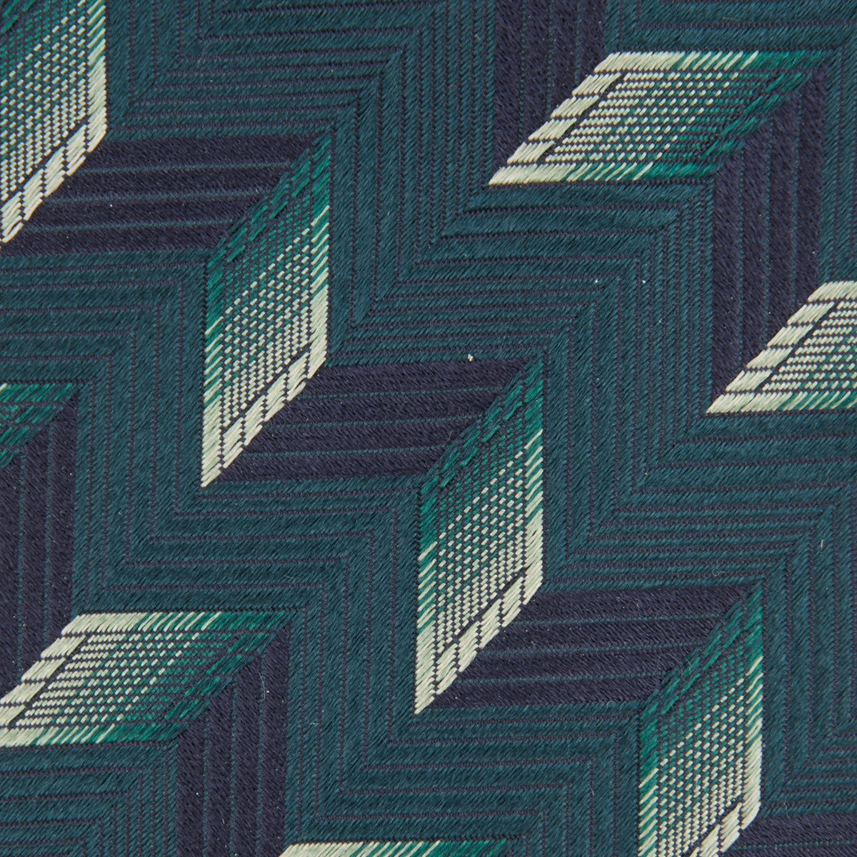 View 3 of product The Turnbull & Asser "The Dark Knight Silk Tie as seen on the Joker" is shown rolled up, featuring a teal zigzag geometric pattern with blue, green, and cream diamonds on a white background.