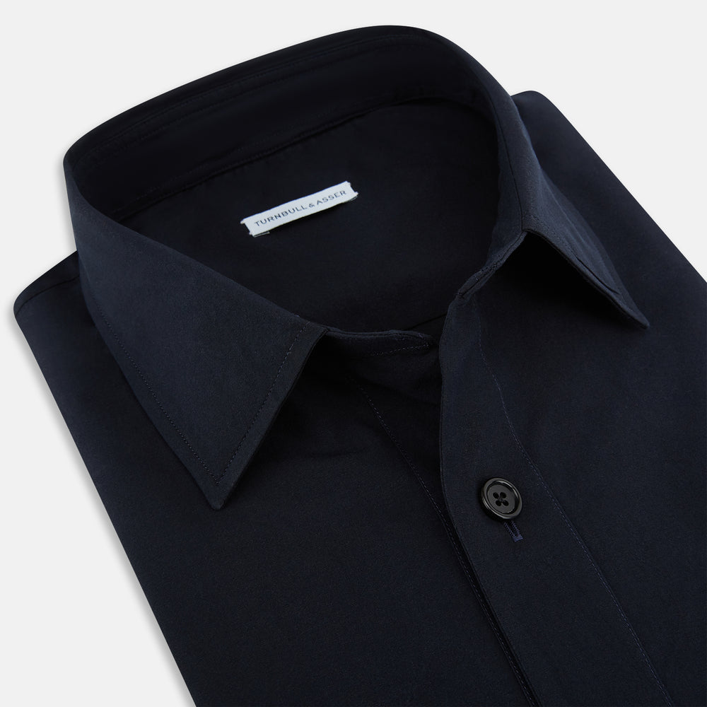 The Midnight Blue Hyde Overshirt by Turnbull & Asser is a plain, long-sleeve shirt in dark navy sanforised cotton with a single chest pocket, spread collar, and black buttons, shown laid flat on a white background.