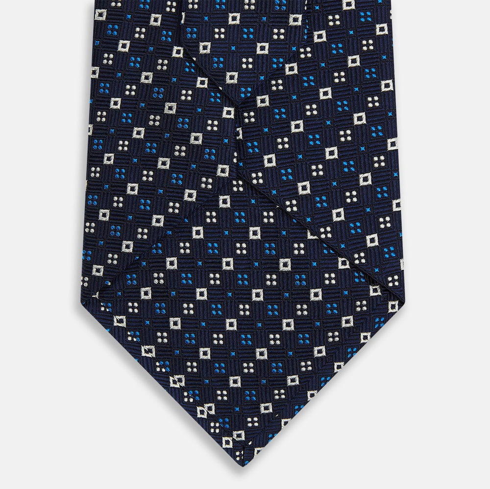 The Blue and White Geometric Silk Tie by Turnbull & Asser, featuring a pattern of small squares and dots, is shown rolled up against a plain white background.