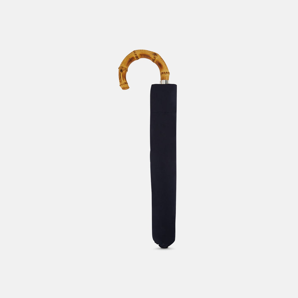 The Turnbull & Asser Navy Telescopic Umbrella with Whangee Crook Handle, featuring a silver shaft, is a refined men's accessory, shown open against a plain white background.