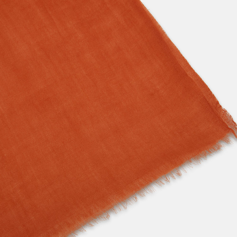 The Rust Cashmere Scarf by Turnbull & Asser is hand-dyed in rust-orange, made from lightweight fabric, tied loosely at the top with both ends hanging down, and finished with subtle frayed edges against a plain white background.