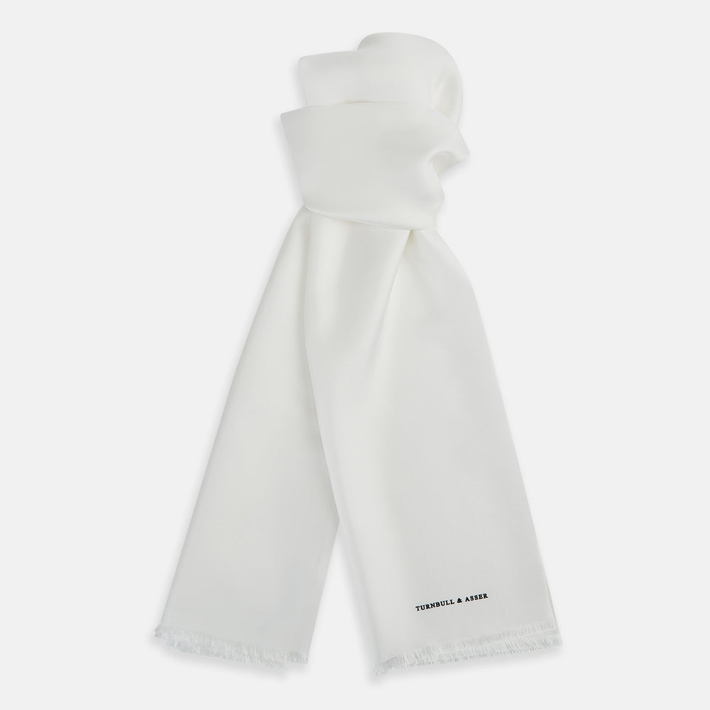 The Turnbull & Asser White Silk Scarf features fringed edges and discreet black branding in the corner, making it a refined accessory for tuxedo jackets or formal wear. Presented neatly folded on a plain white background.