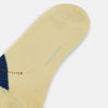 View 3 of product The Turnbull & Asser Vanilla Wool Check Mid-Length Sock is beige with blue, black, and white argyle diamonds on the side and solid beige toe, heel, and cuff. Displayed on a plain white background.