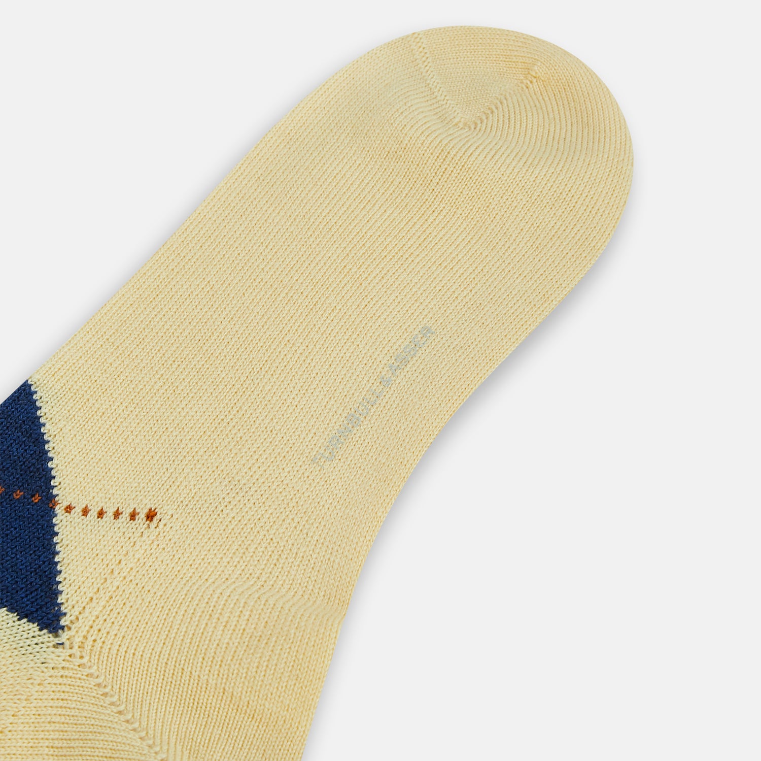 View 3 of product The Turnbull & Asser Vanilla Wool Check Mid-Length Sock is beige with blue, black, and white argyle diamonds on the side and solid beige toe, heel, and cuff. Displayed on a plain white background.