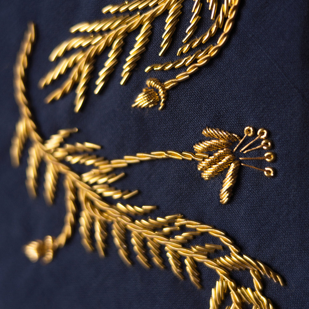 The Turnbull & Asser Navy Gold Embroidered Botanical Tie features intricate gold botanical embroidery on navy blue silk, neatly rolled with the detailed tip facing forward.