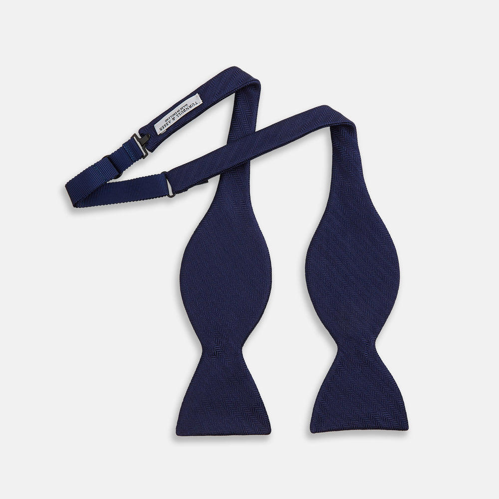 The Turnbull & Asser HERRINGBONE NAVY BOW TIE features a subtle herringbone pattern in navy blue, shown against a plain white background—the perfect accessory to elevate any smart look.