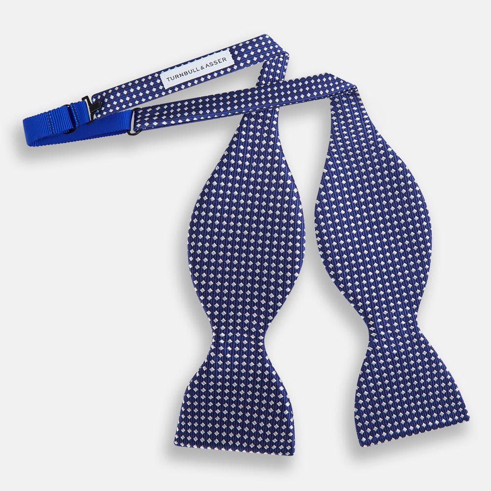 The Turnbull & Asser Blue and White Diamond Silk Bow Tie features a repeating pattern of small white diamonds and vertical ribbing, making it perfect for formalwear. Displayed on a white background.