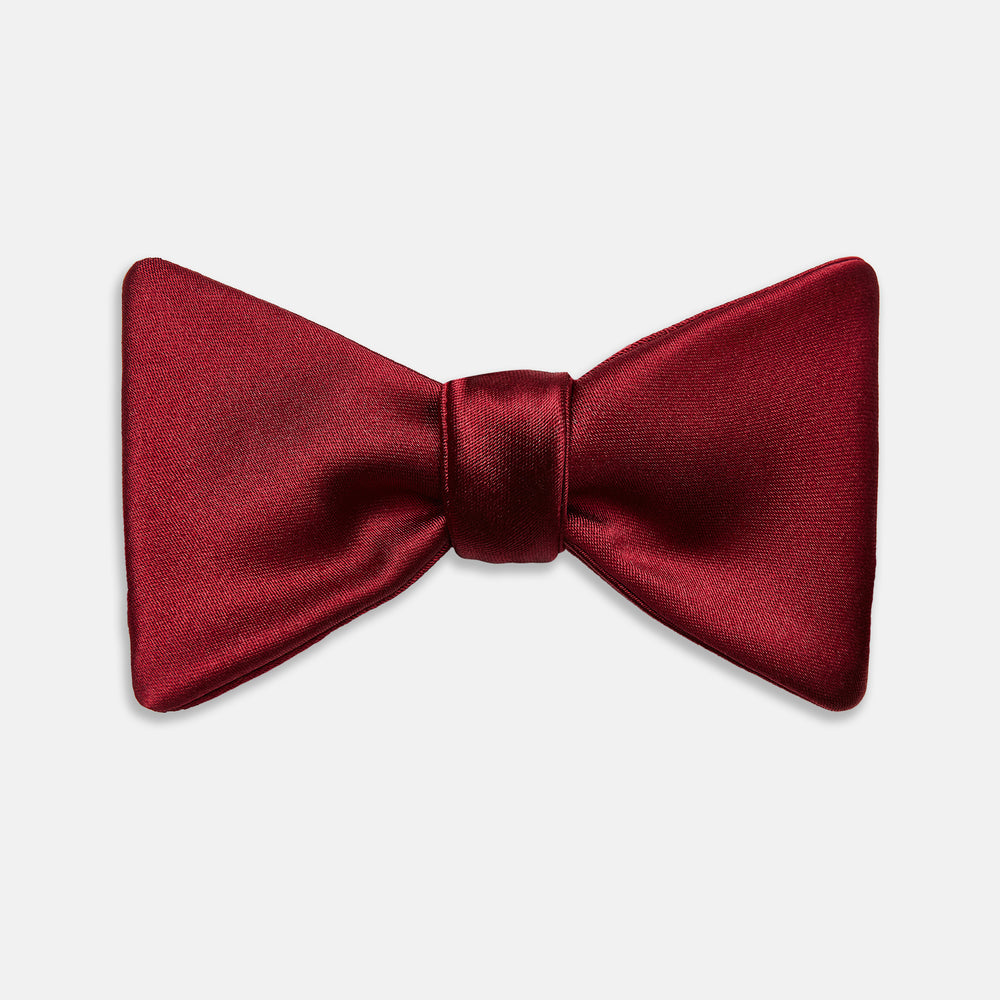 The Turnbull & Asser BURGUNDY SATIN BOW TIE features a deep red, smooth, and shiny finish—an essential accessory—neatly tied and showcased against a plain white background.