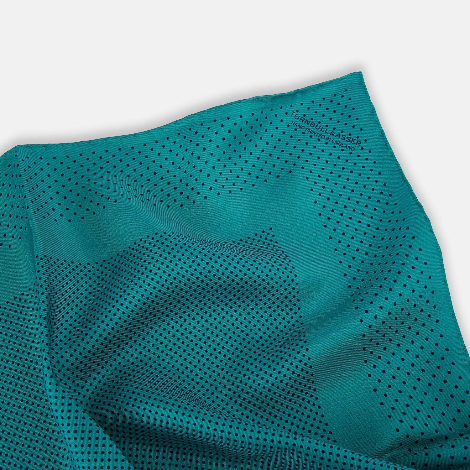 View 2 of product The Turnbull & Asser Petrol Green Dot Silk Pocket Square, made in England, features a border and small black polka dots, neatly folded to showcase both front and back sides.