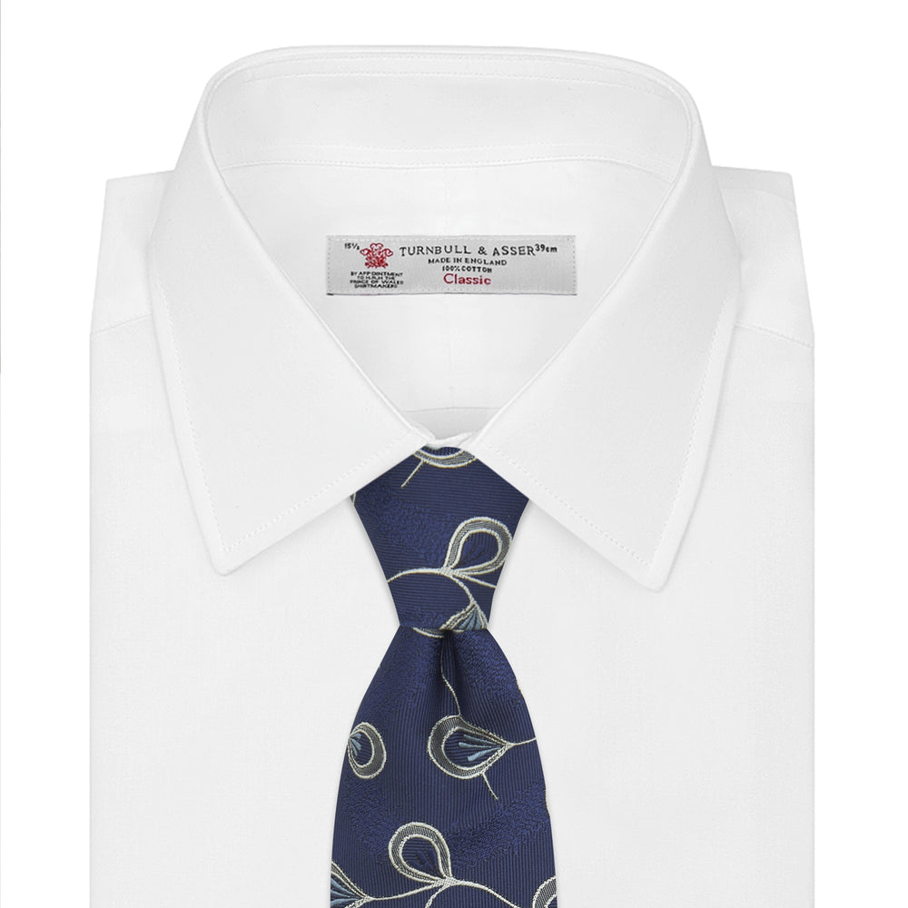 The Turnbull & Asser Navy Jacquard Silk Floral Tie features white and light blue abstract leaf designs, exemplifying fine British craftsmanship. Shown rolled up against a white background.