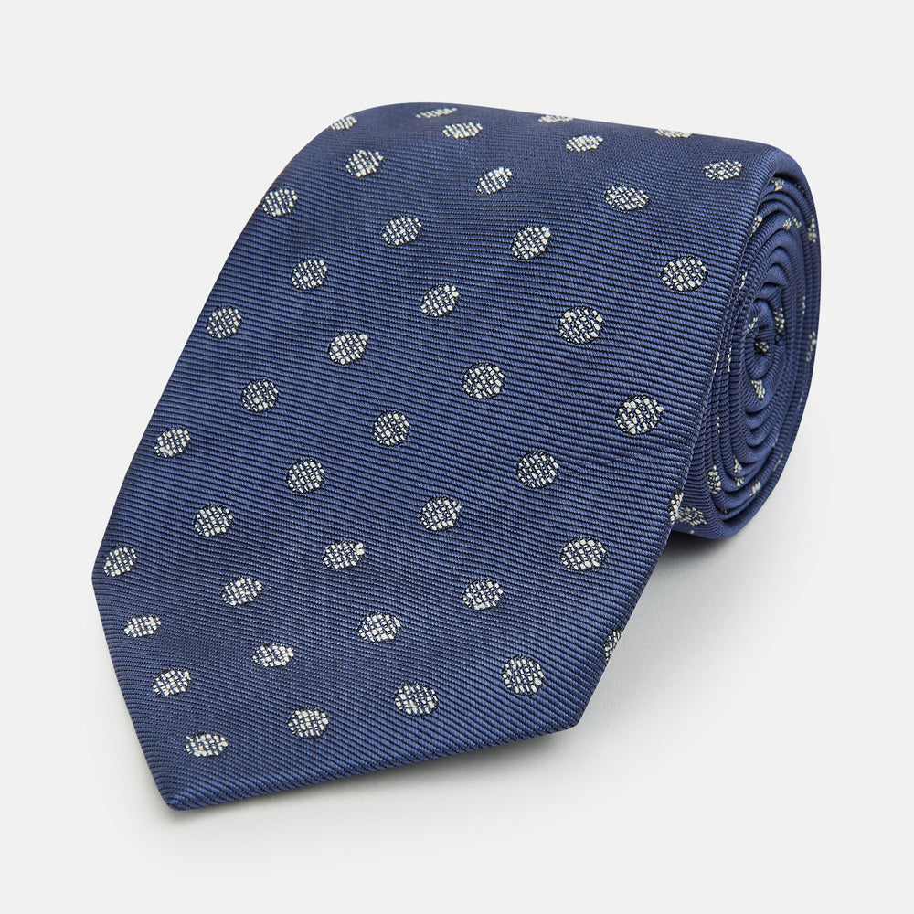 The Turnbull & Asser Navy Circle Silk Tie, made from pure silk with a navy base and small white dot pattern, is shown rolled up on a plain white background.
