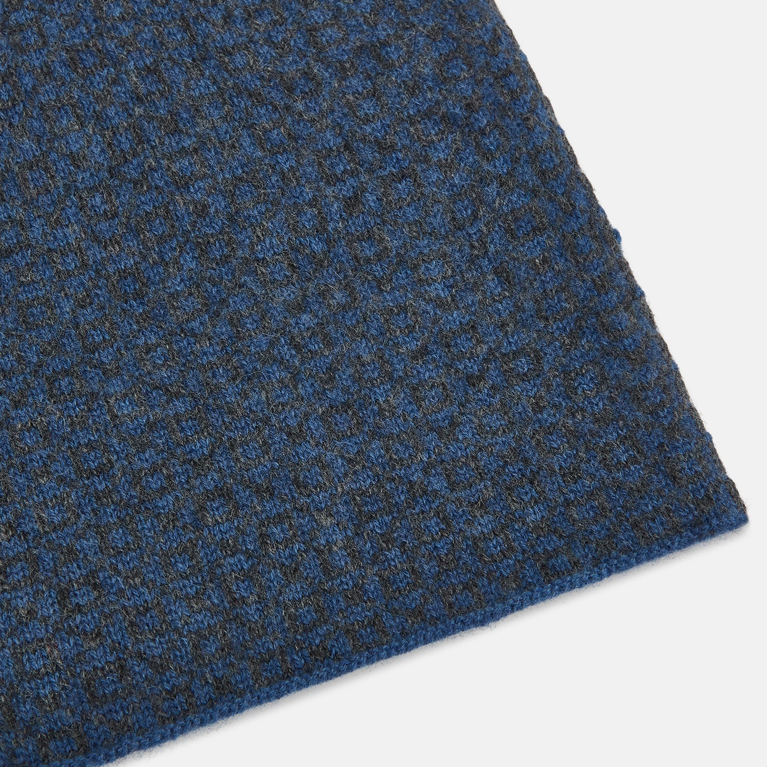 View 2 of product The Azzurro and Graphite Lozenge-Patterned Cashmere Knitted Scarf by Turnbull & Asser features a blue geometric design and luxurious softness, displayed in a looped drape with both ends hanging against a white background.