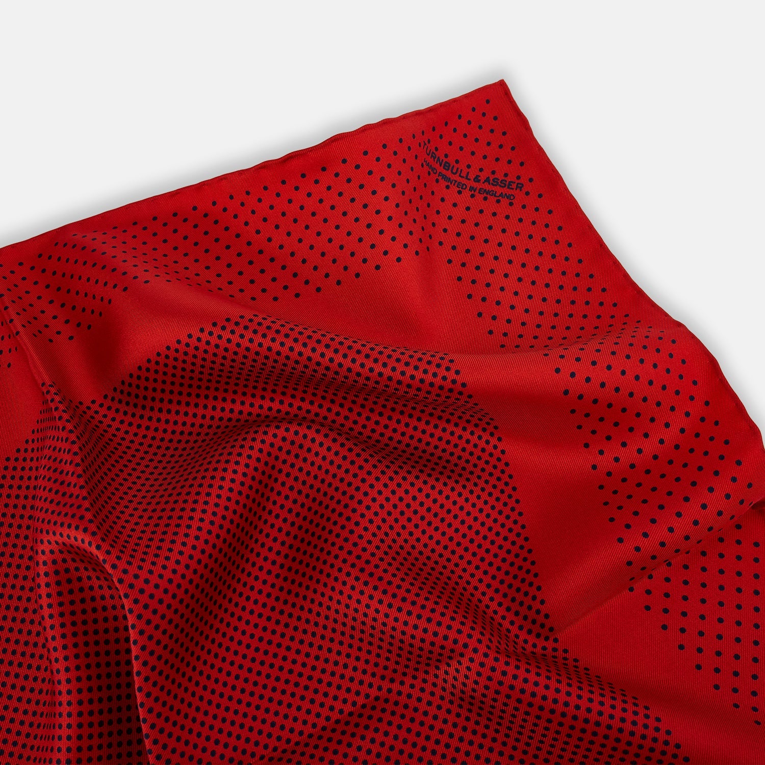 View 2 of product The Turnbull & Asser Red Dot Silk Pocket Square showcases small black dots on red silk, neatly folded to reveal both the front and part of the reverse side.