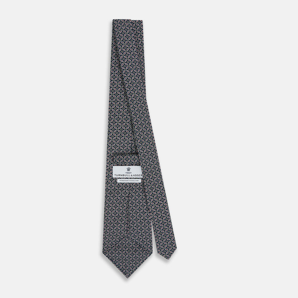 The Turnbull & Asser Navy Mélange Paisley and Square Print Silk Tie is crafted from fine silk, showcasing a repeating paisley and square pattern in blue tones, elegantly rolled for display on a white background.