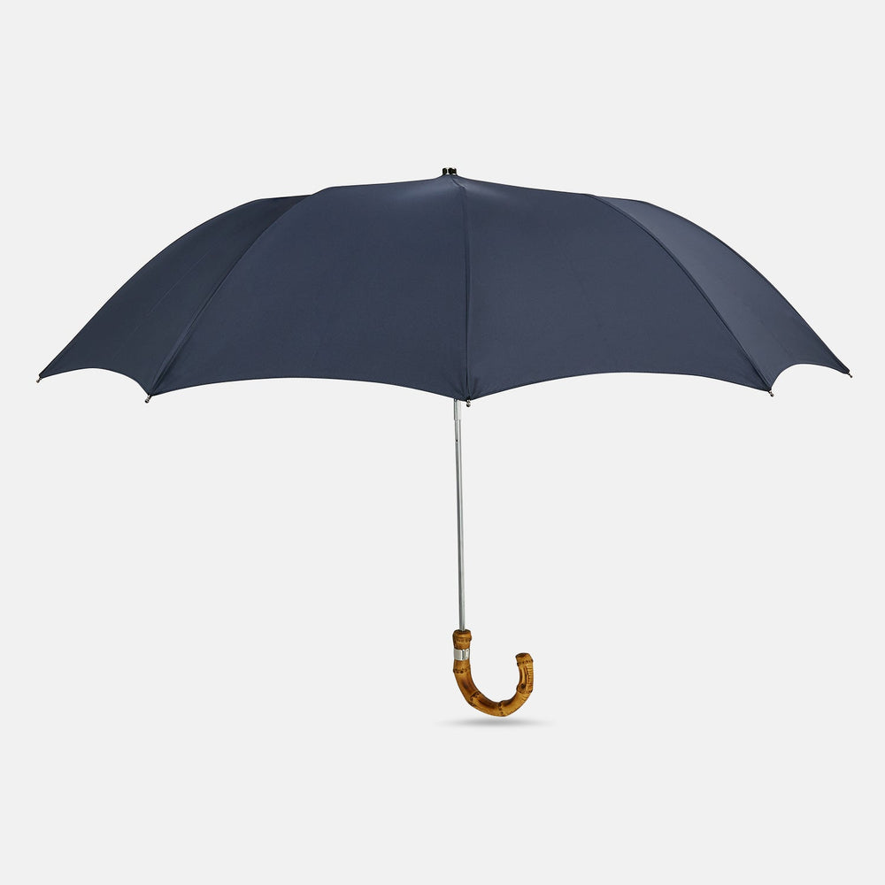 The Turnbull & Asser Navy Telescopic Umbrella with Whangee Crook Handle, featuring a silver shaft, is a refined men's accessory, shown open against a plain white background.