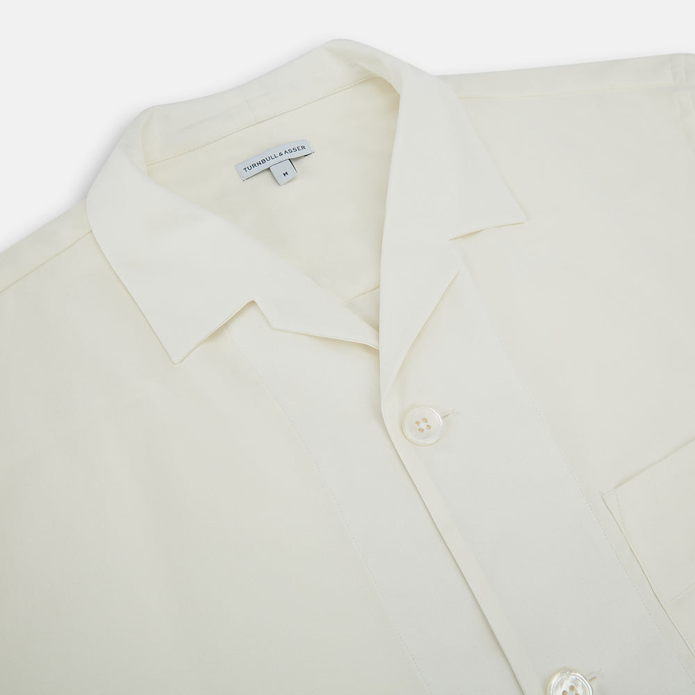 The Turnbull & Asser Cream Silk Pyjama Set, shown laid flat on a white background, features a long-sleeve button-up top with a chest pocket and matching pants with an elastic drawstring waist—ideal for comfortable loungewear.